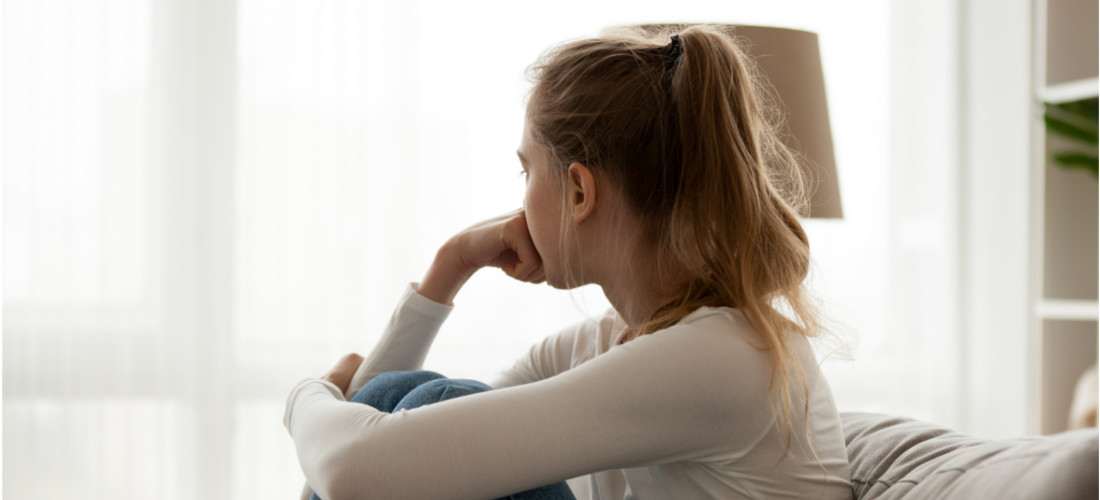 Auf dem Bild sitzt ein Mädchen auf dem Sofa und schaut mit dem Gesicht zum GFenster. Man kann ihren Rücken sehen. Den Kopf stützt sie mit der Hand ab.