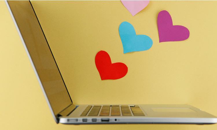 Geöffneter Laptop vor einer gelben Wand mit bunten Herzen.