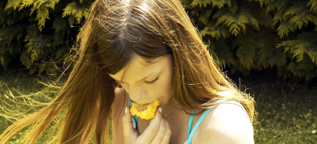 Das Foto zeigt ein Mädchen, das nach unten schaut und dabei in eine Frucht beißt.