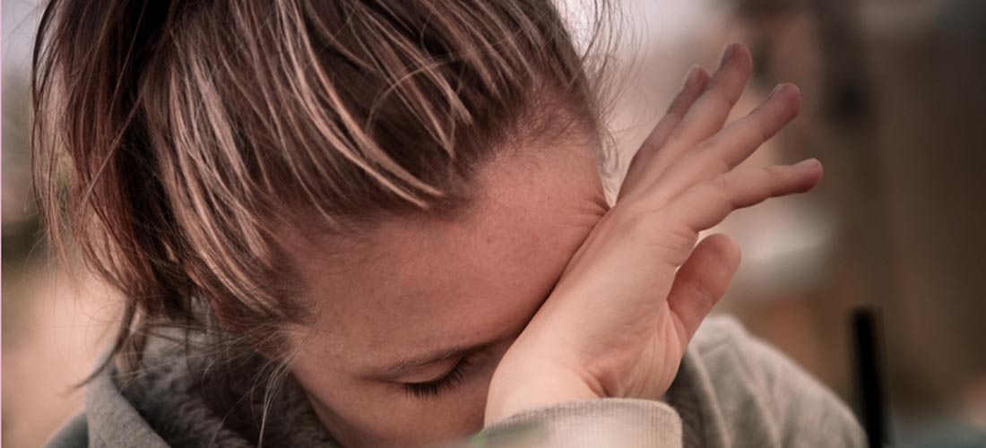 Das Foto zeigt eine junge Frau, die ihren Handrücken vor ihr Gesicht hält und zu Boden schaut. Sie wirkt niedergeschlagen.