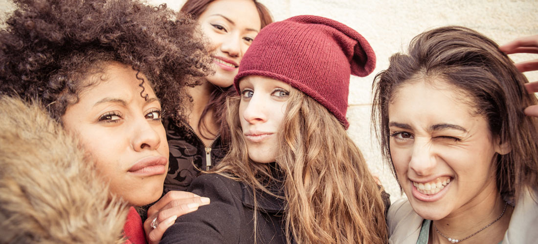 Das Foto zeigt eine Gruppe von vier Mädchen: Das Mädchen links guckt skeptisch in die Kamera, das Mädchen daneben lächelt freundlich, die beiden Mädchen links machen freche Grimassen.