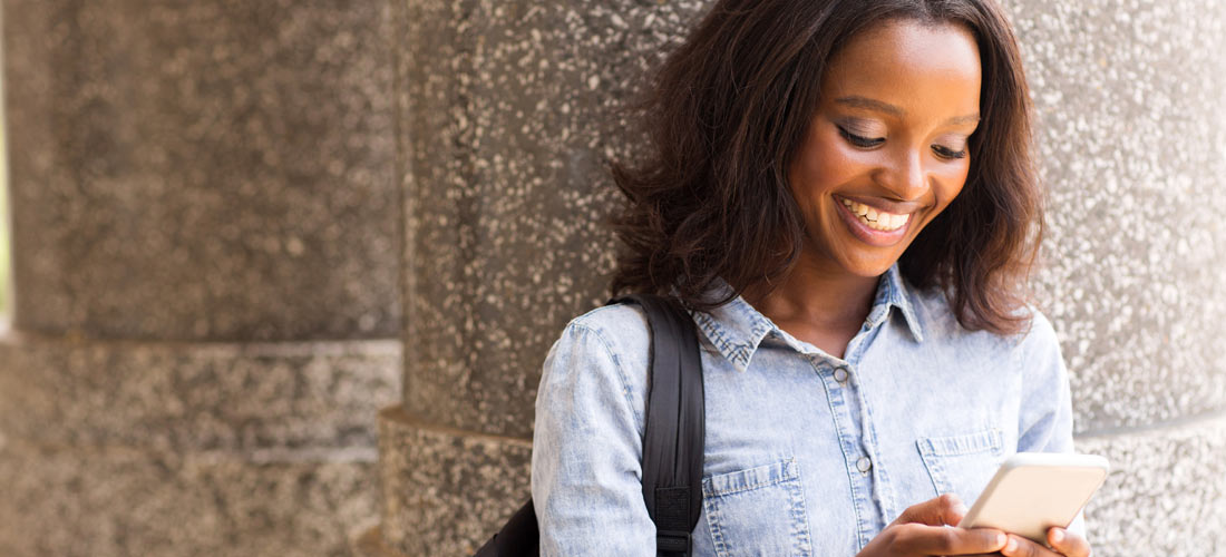 Schwarzes Mädchen, das lächelt und mit dem Smartphone hantiert