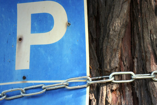 Das Foto zeigt ein Parkplatz-Schild, das mit einer Kette an einen Baum befestigt wurde.